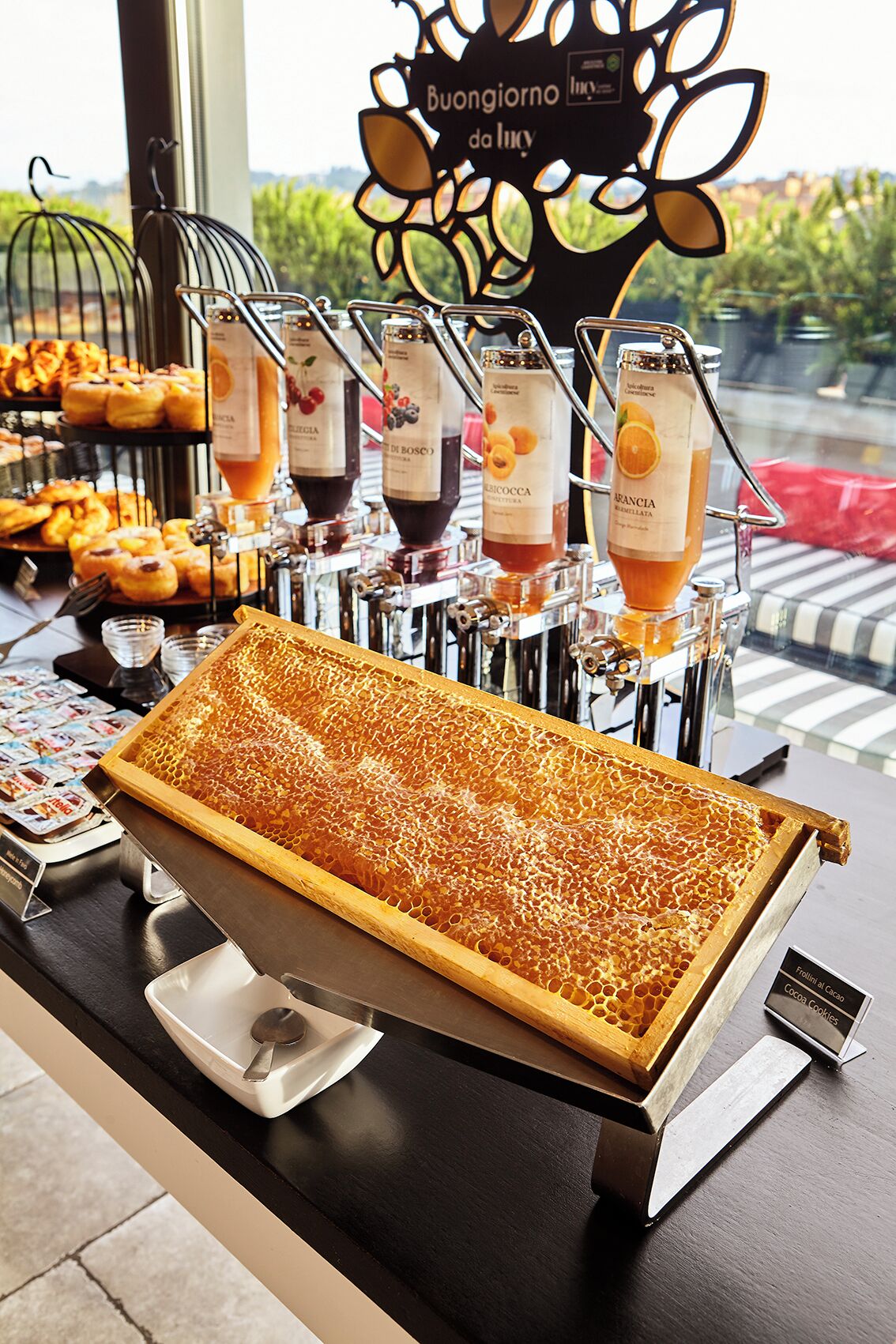 A buffet with a honeycomb centerpiece, various pastries, and labeled drink dispensers.