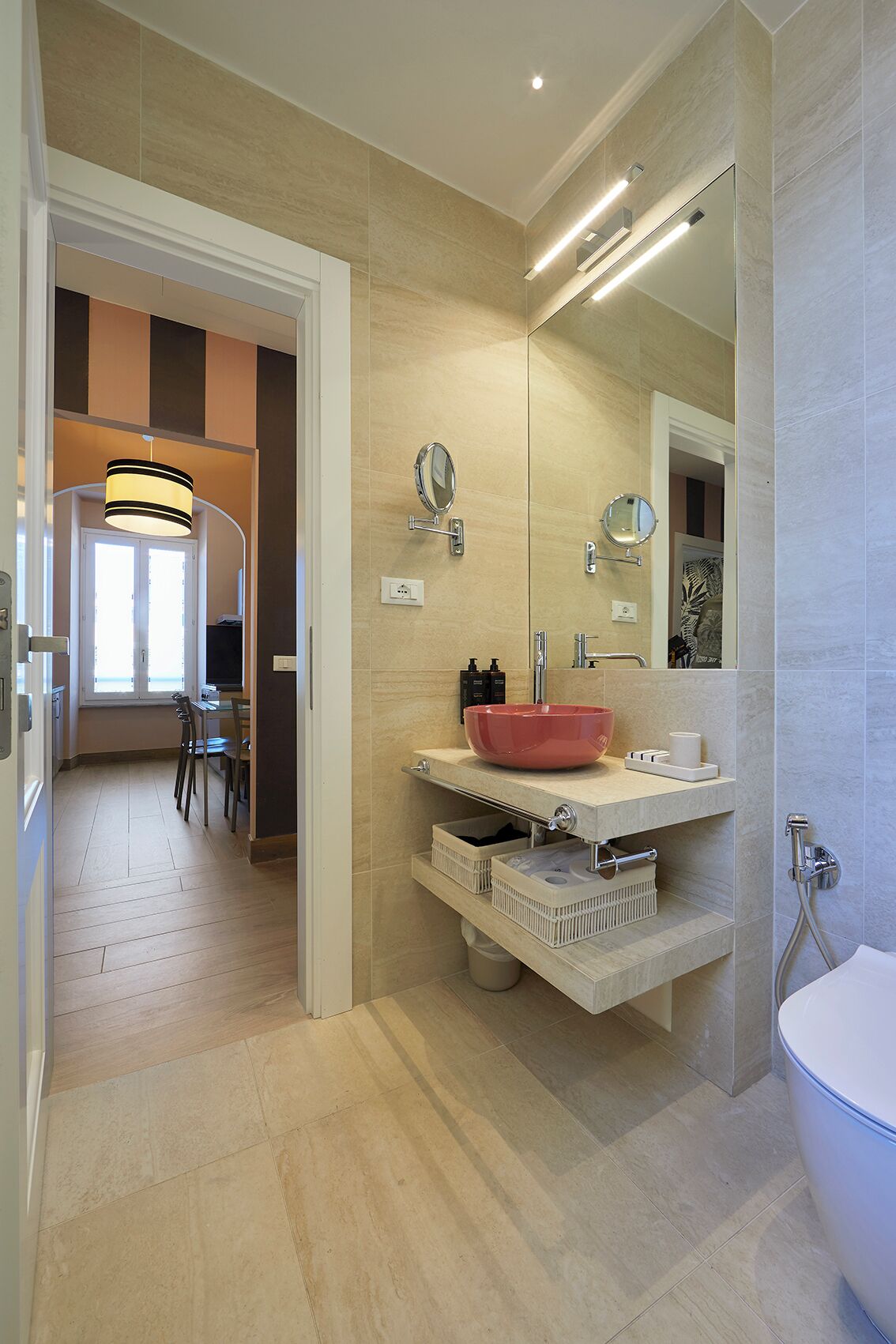 A modern bathroom with a large mirror, a red basin, and a shower.