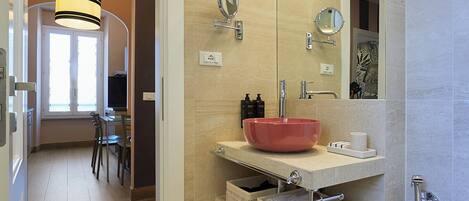 A modern bathroom with a large mirror, a red basin, and a shower.