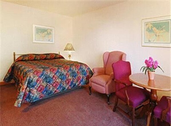 A hotel room with a bed, a chair, a table, and a vase with flowers. - The Atlantic Motel (East Wareham)