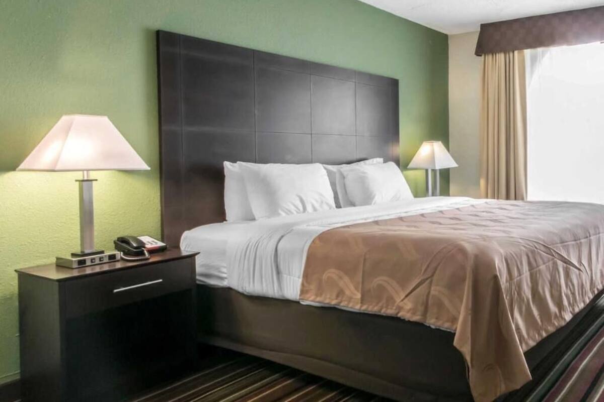 A hotel room with a bed, bedside lamps, a nightstand, and a window with curtains.