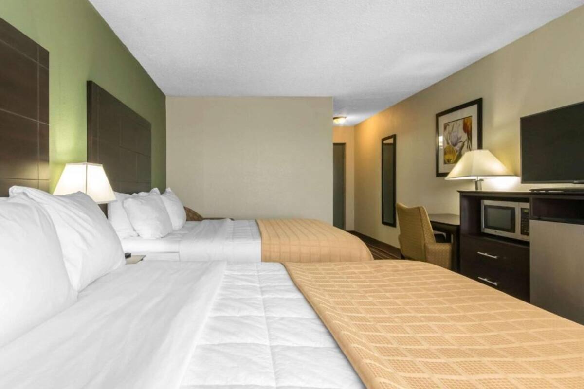 A hotel room with two beds, a desk, a chair, a television, and a microwave.