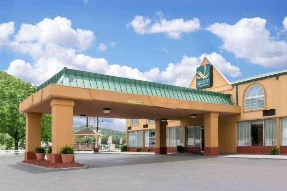 A hotel with a covered entrance, a sign with a logo, and a large window.