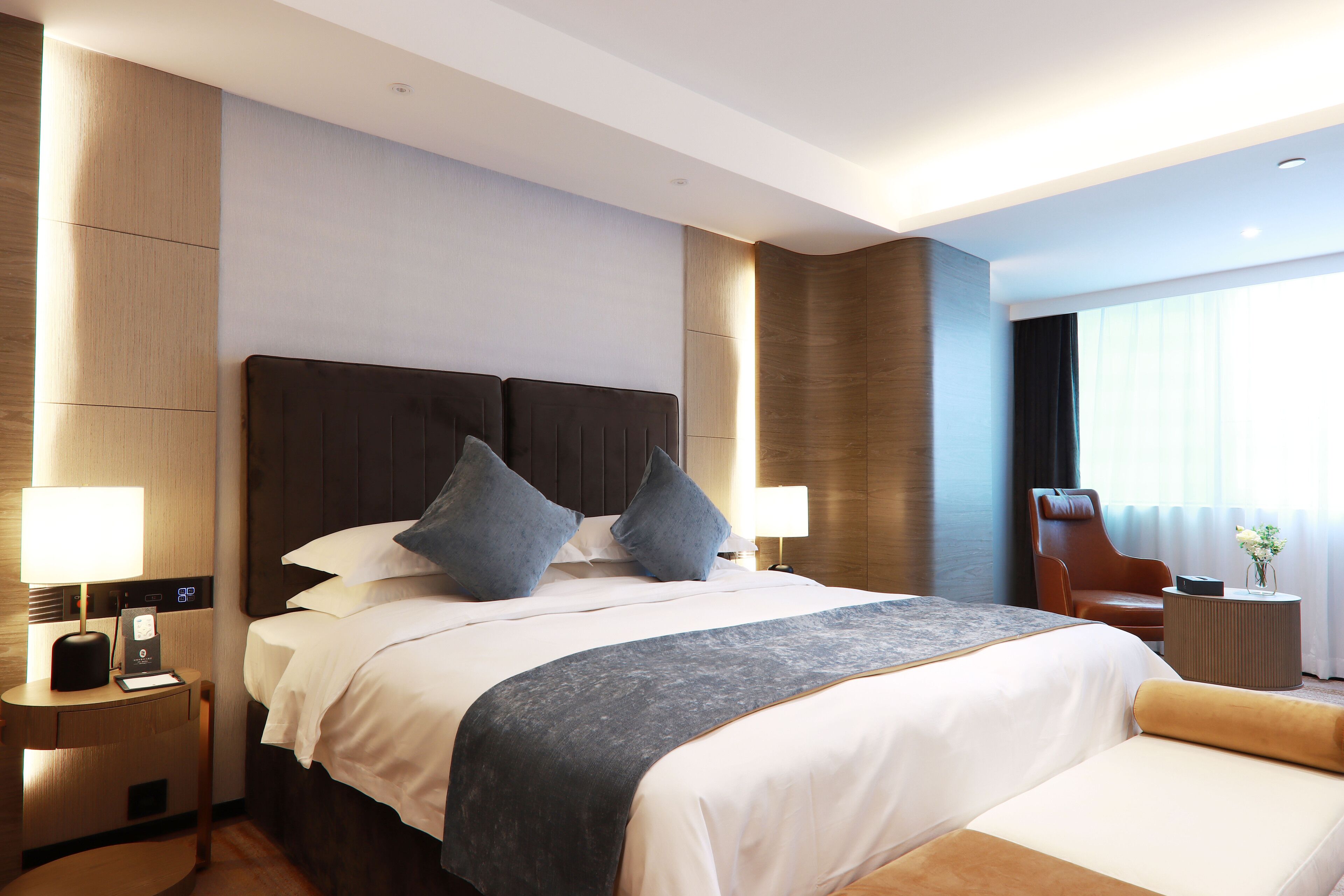 Ein modernes Hotelzimmer mit einem großen Bett, zwei Nachttischen, einem Sessel und einem Fenster mit Vorhängen.