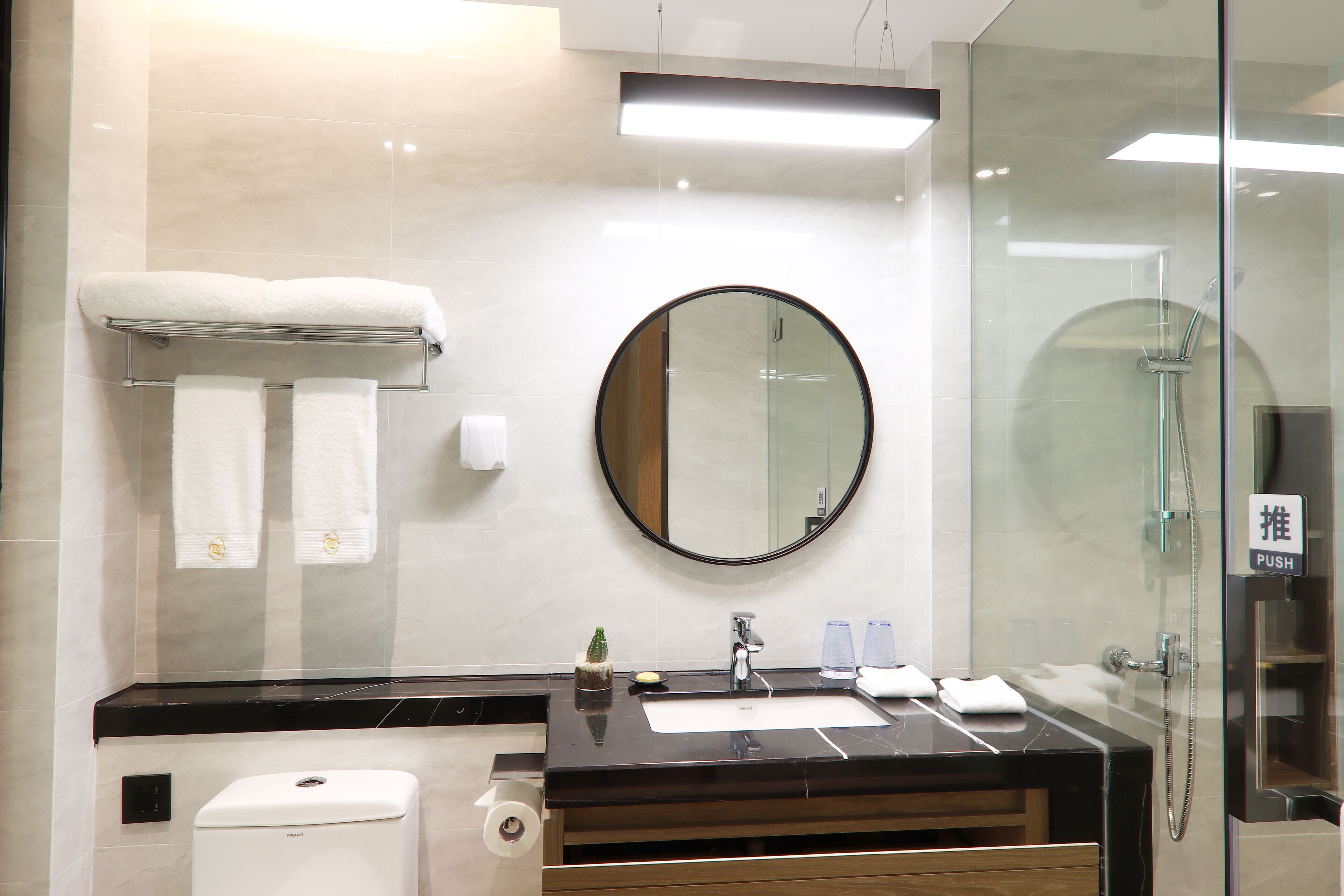 Une salle de bain moderne avec un plan de toilette noir, un miroir rond et une douche à parois de verre.