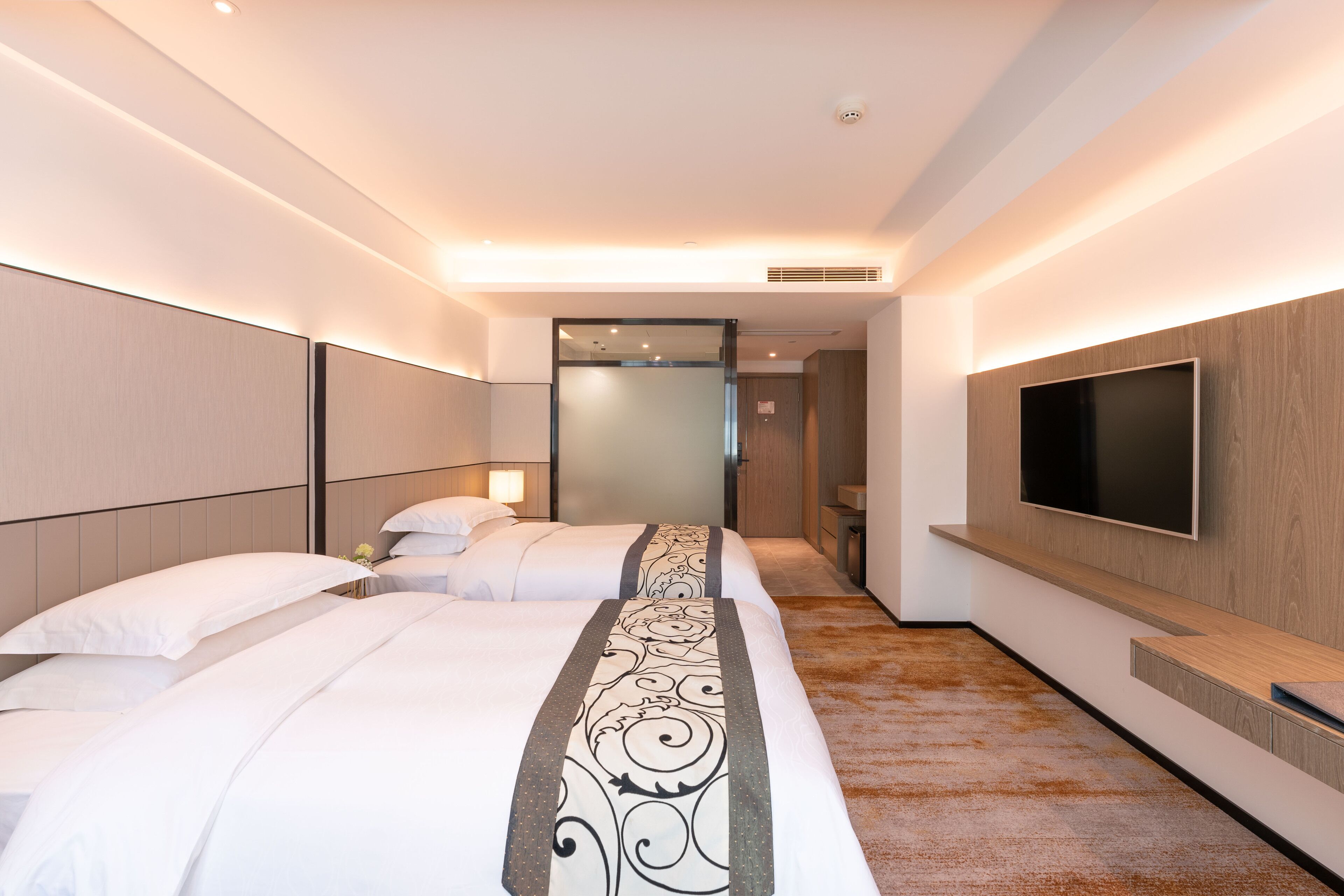 A hotel room with two beds, a TV mounted on the wall, and a carpeted floor.