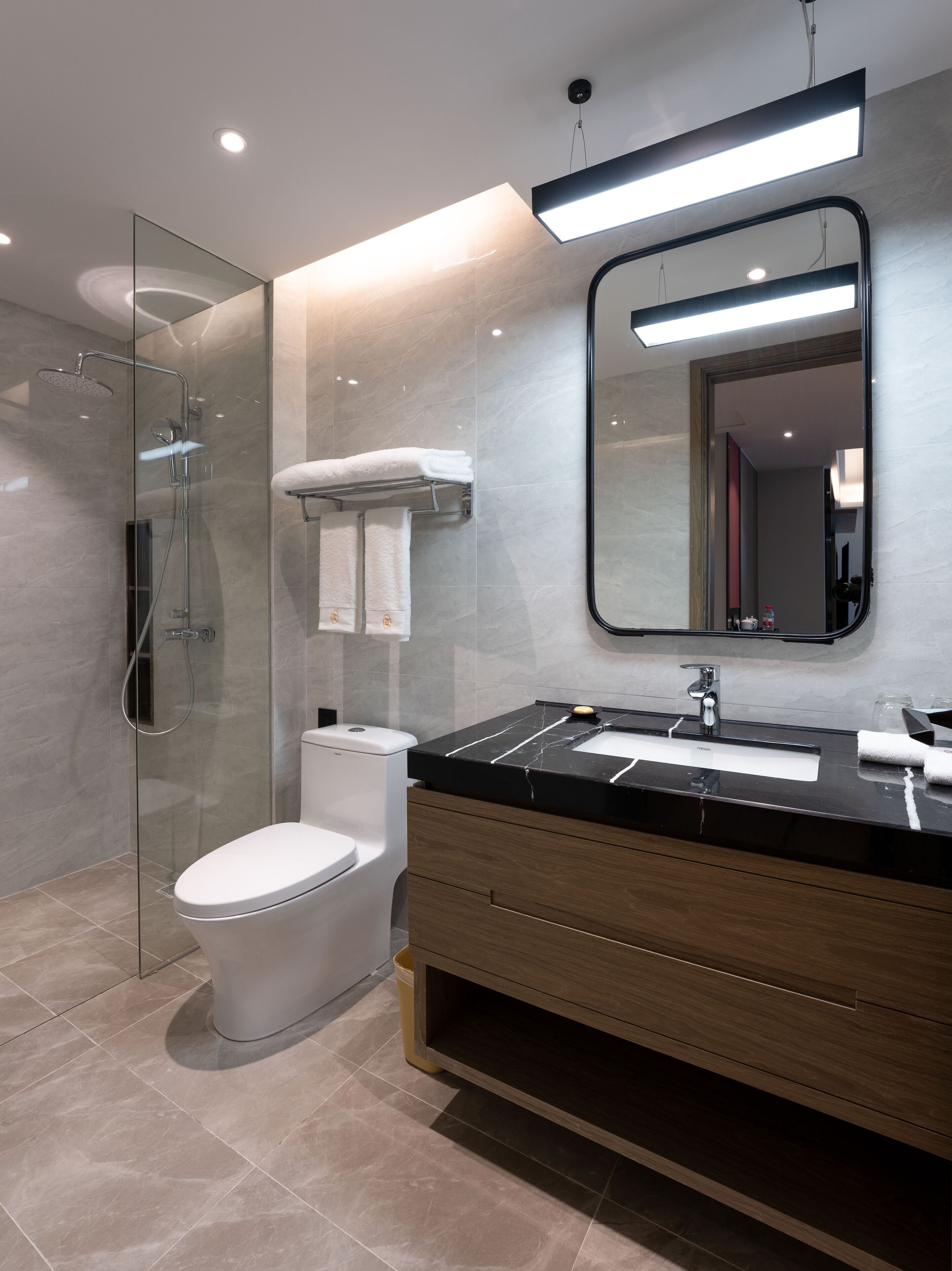 A modern bathroom with a glass-enclosed shower, a white toilet, a black marble sink, and a wooden vanity.