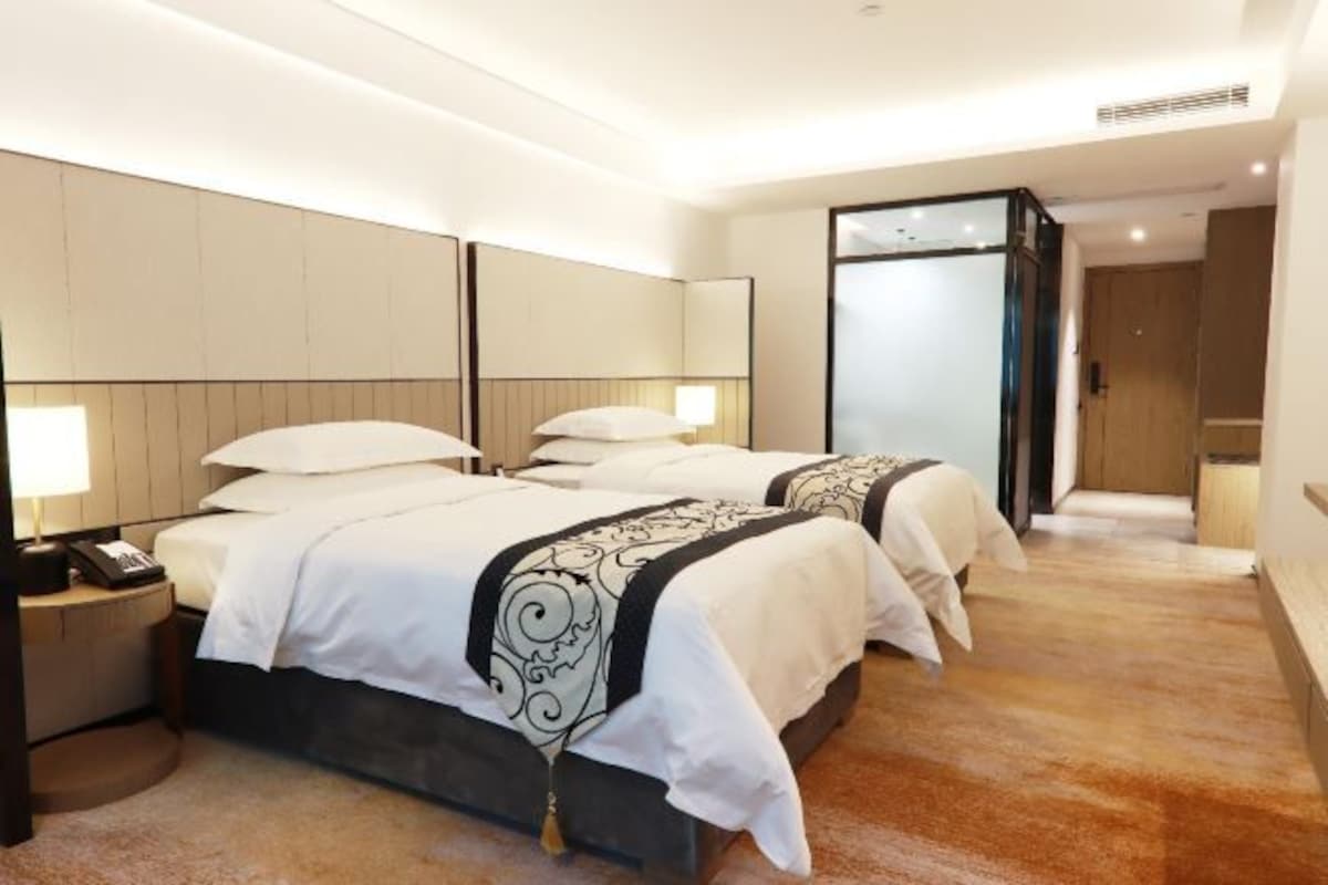 A hotel room with two beds, a bedside table with a lamp, and a large mirror.