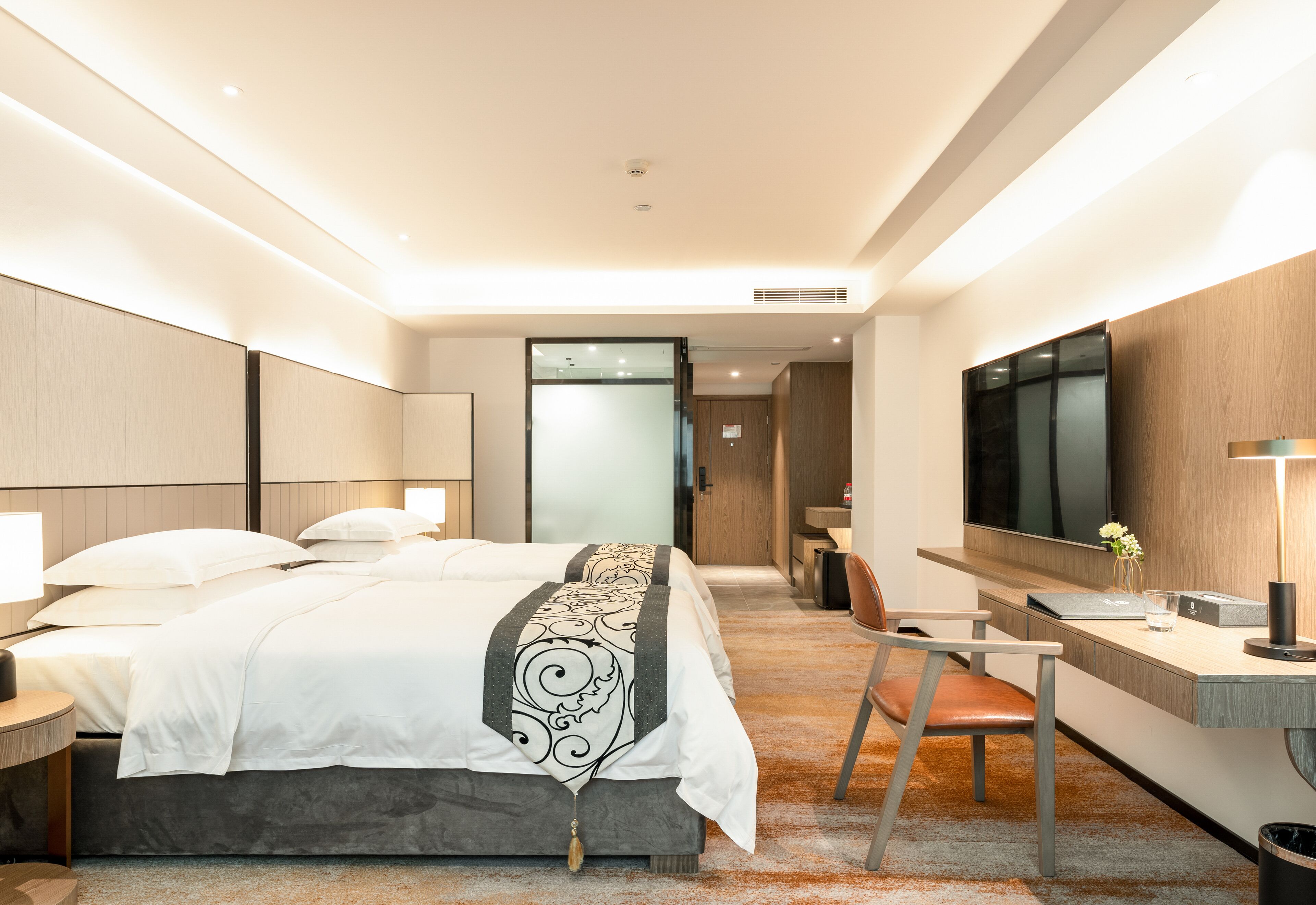 A modern hotel room with a large bed, a desk, a chair, and a TV.
