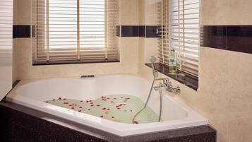 Un baño moderno con una bañera independiente, un cabezal de ducha manual y pétalos de rosa en el agua.