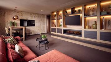 Een moderne woonkamer met een grote televisie, inbouwkasten met decoratieve objecten, een rode bank en een klein, rond tafeltje.