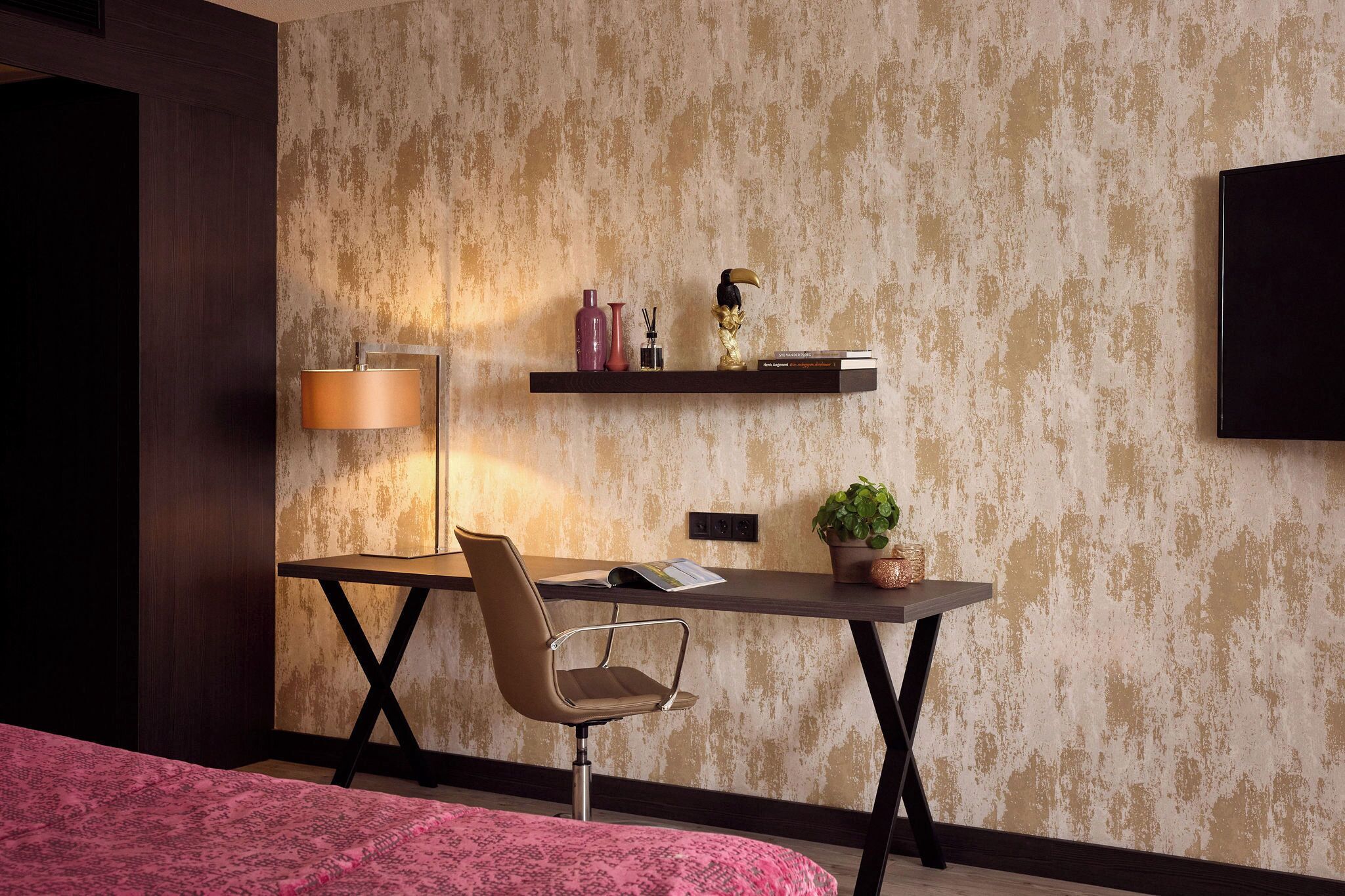 Una habitación de hotel moderna con escritorio, silla y cama con cubrecama rosa.