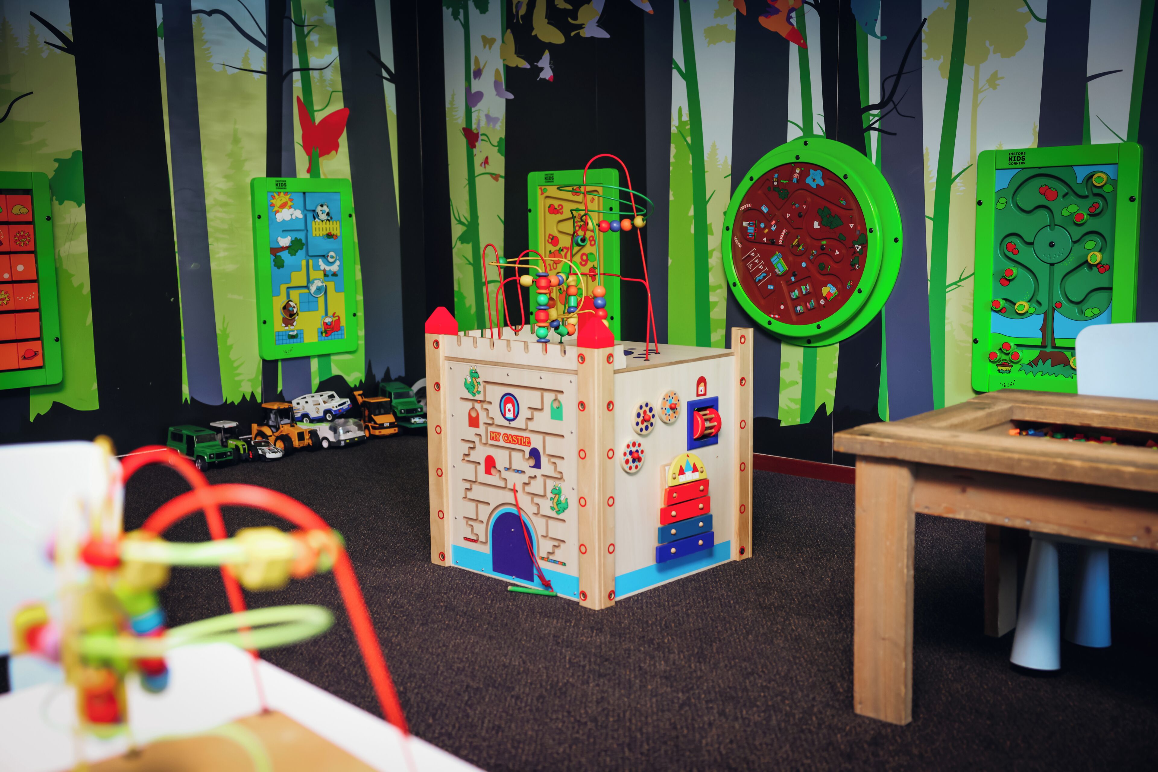 Een speelruimte met een speelconstructie in kasteelthema, een tafel en educatieve wanddecoraties.