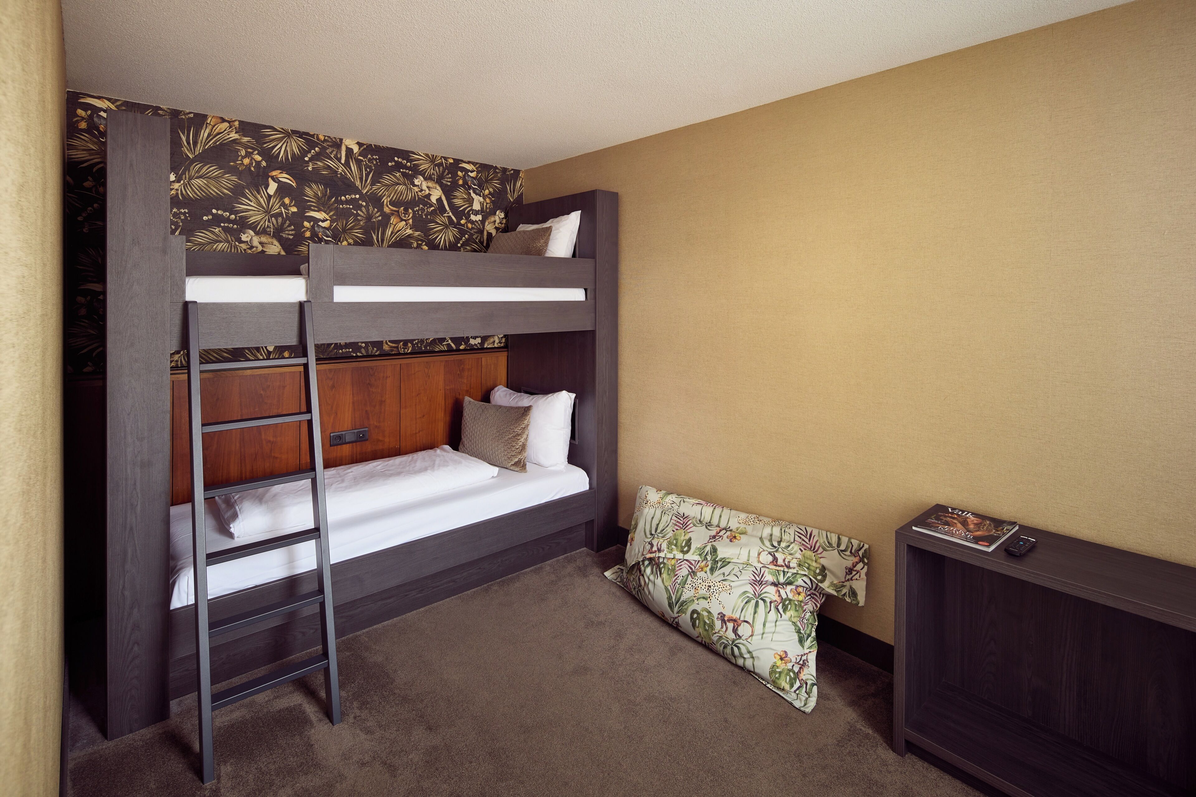 A bunk bed with a ladder, a wooden headboard, a bedside table, and a patterned pillow.