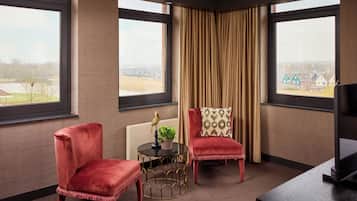 Una habitación con dos sillones de terciopelo rojo, una mesita redonda con una planta y una estatua de pájaro, y un televisor sobre un mueble de madera.