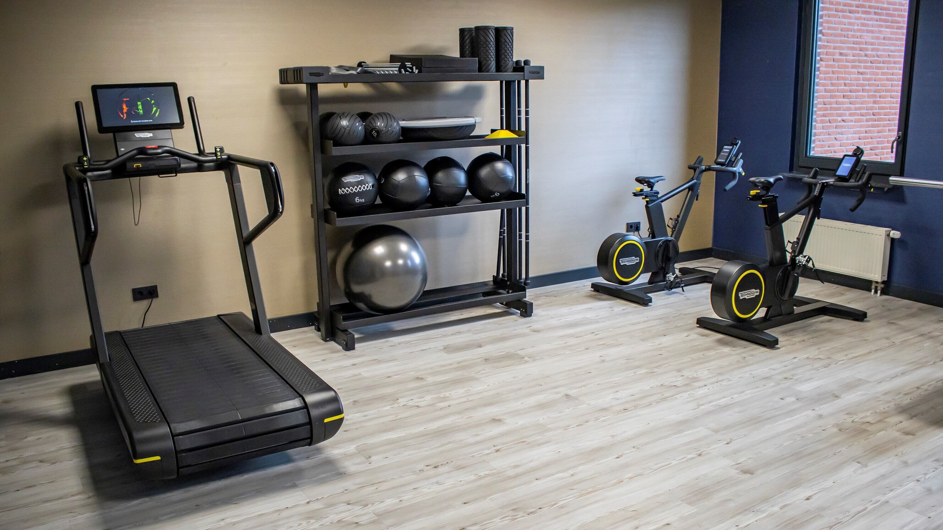 Een sportschool met een loopband, gewichtsschijven en een hometrainer.