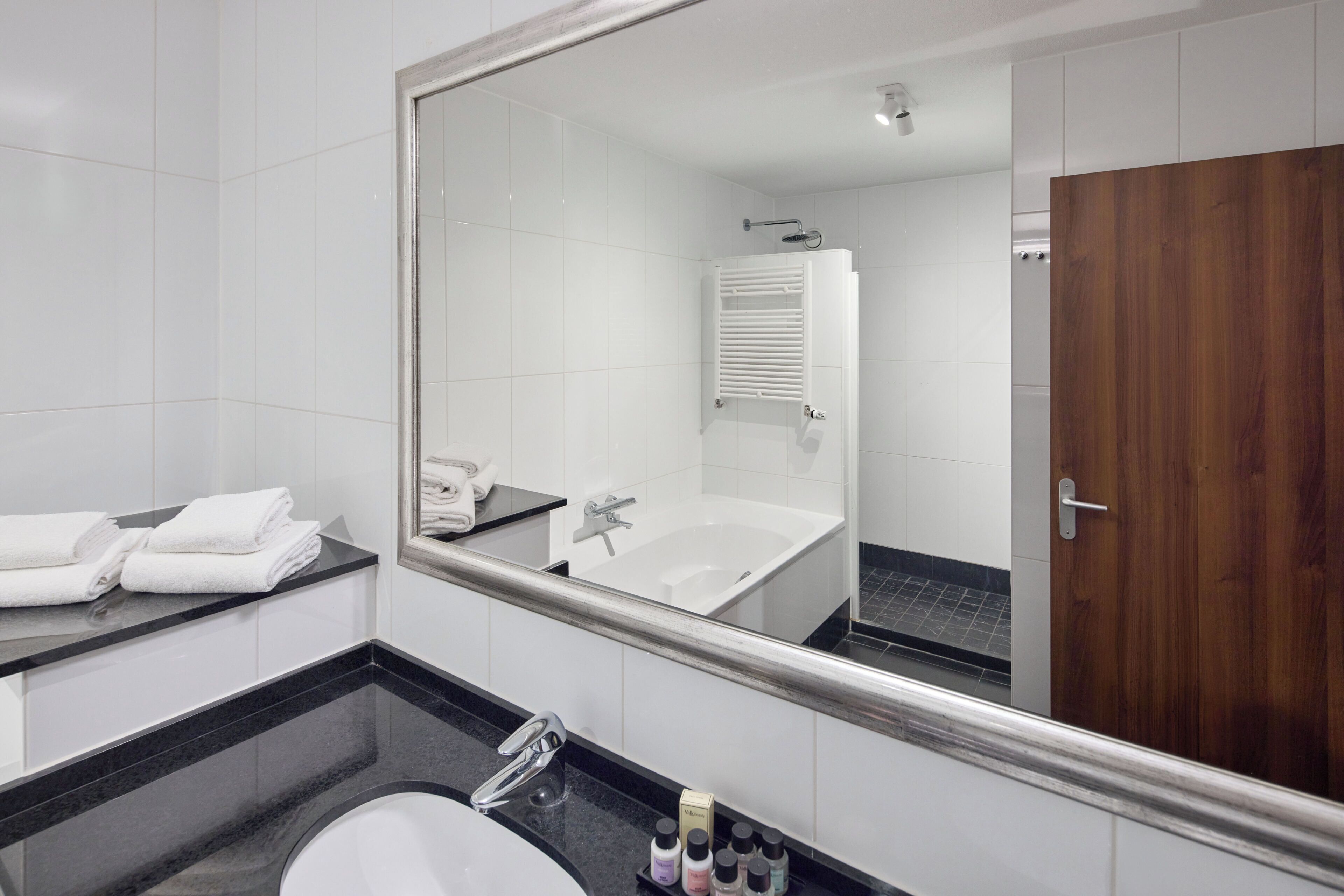 Un baño moderno con un espejo grande, un lavabo, una bañera y una puerta de madera.