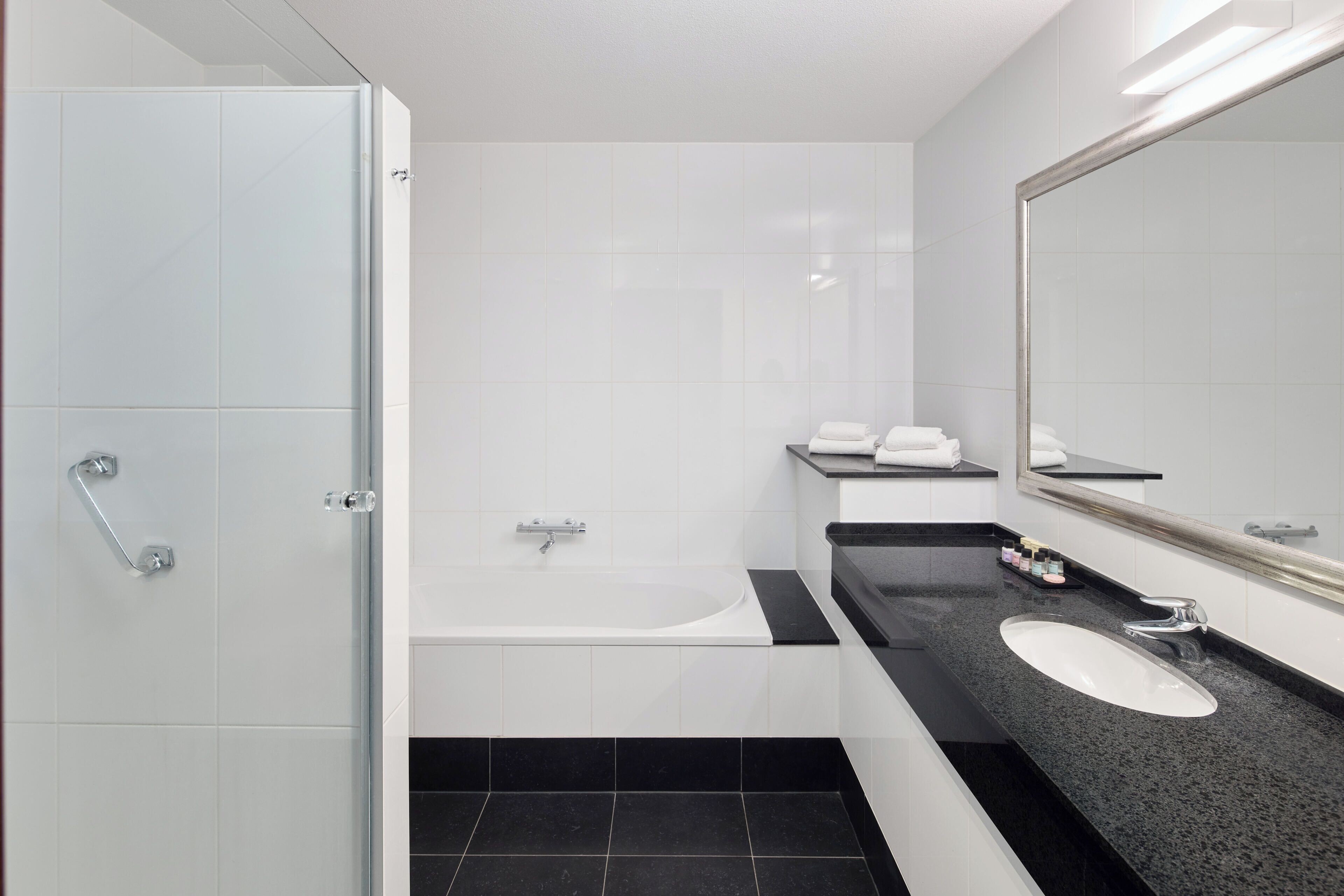 A modern bathroom with a glass shower enclosure, a white bathtub, a black countertop sink, and a large mirror.