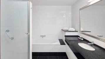 A modern bathroom with a glass shower enclosure, a white bathtub, a black countertop sink, and a large mirror.