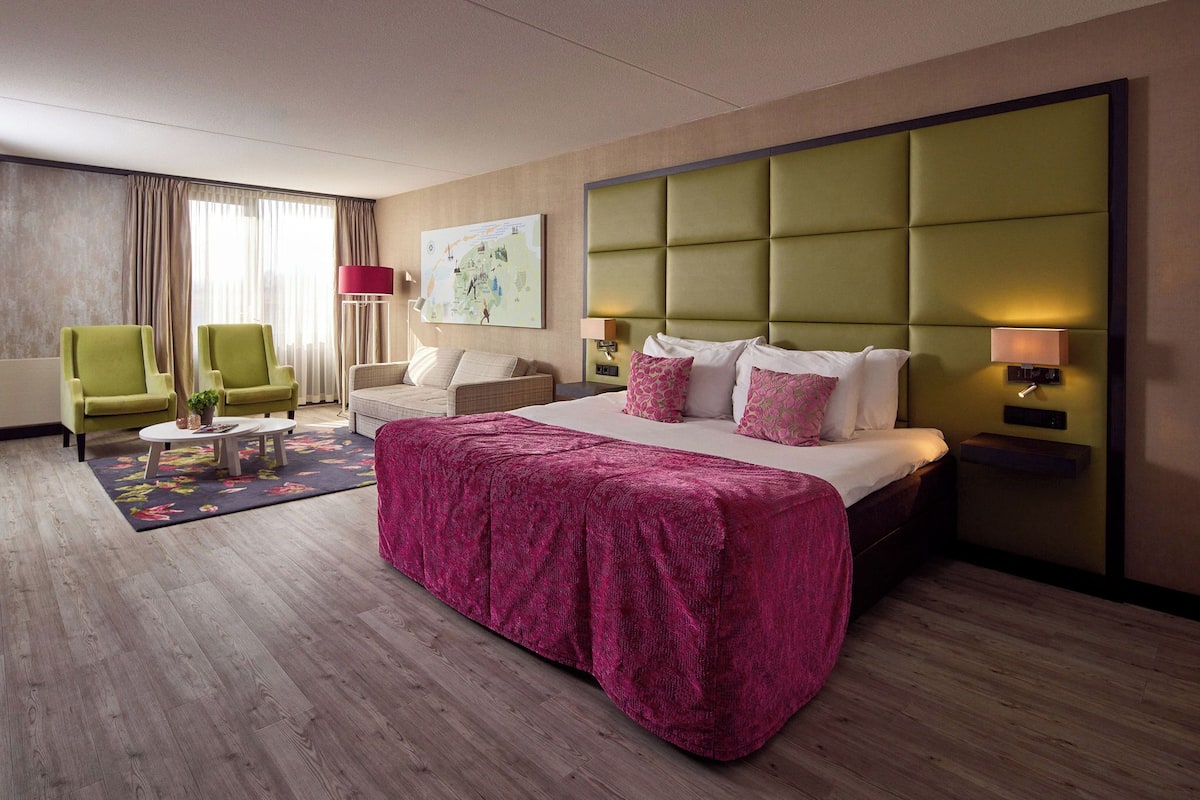 Una habitación de hotel con una cama grande, un sillón verde, un sofá, una mesita y un mapa en la pared.