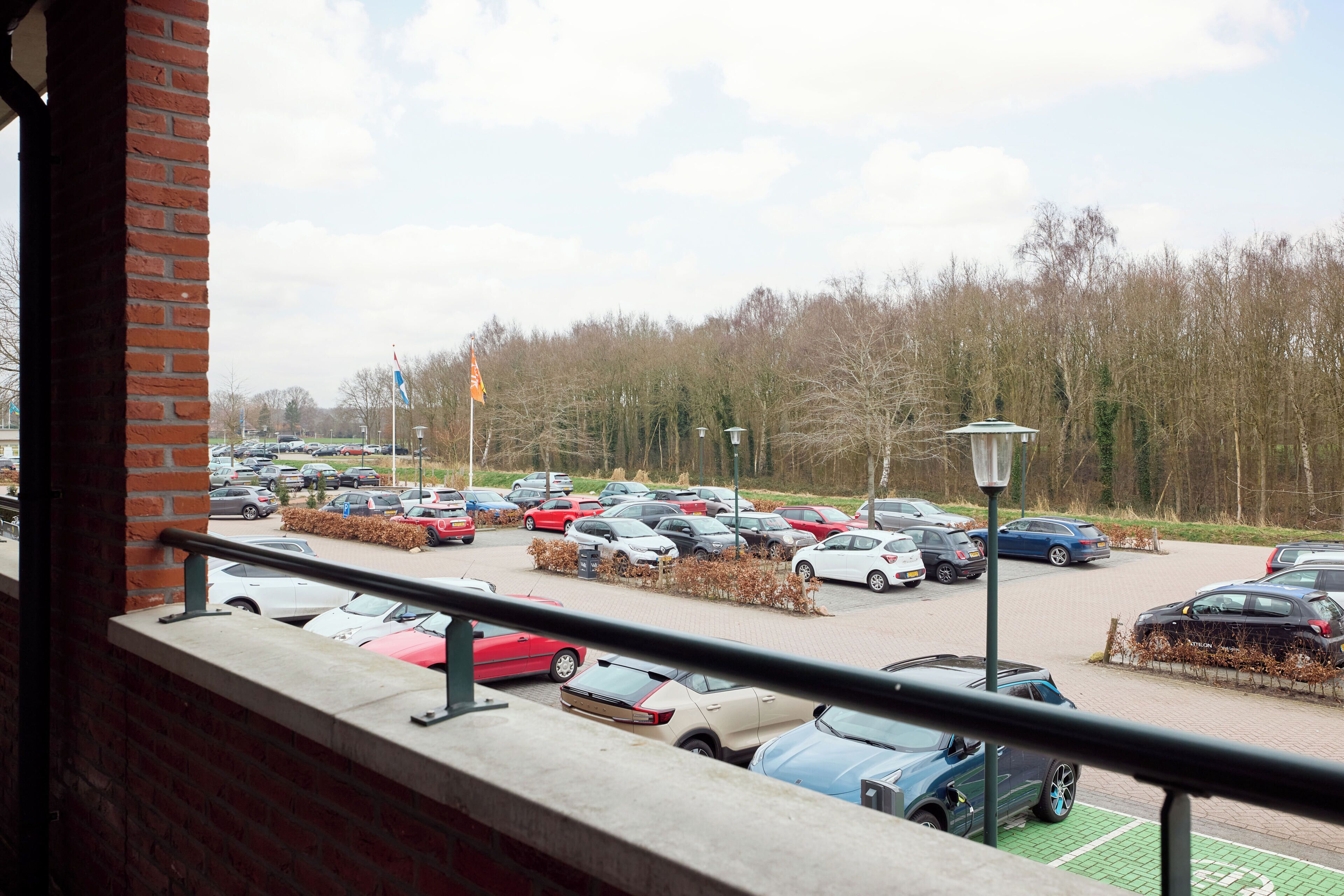 Um estacionamento com vários carros, uma parede de tijolos e um guarda-corpo.