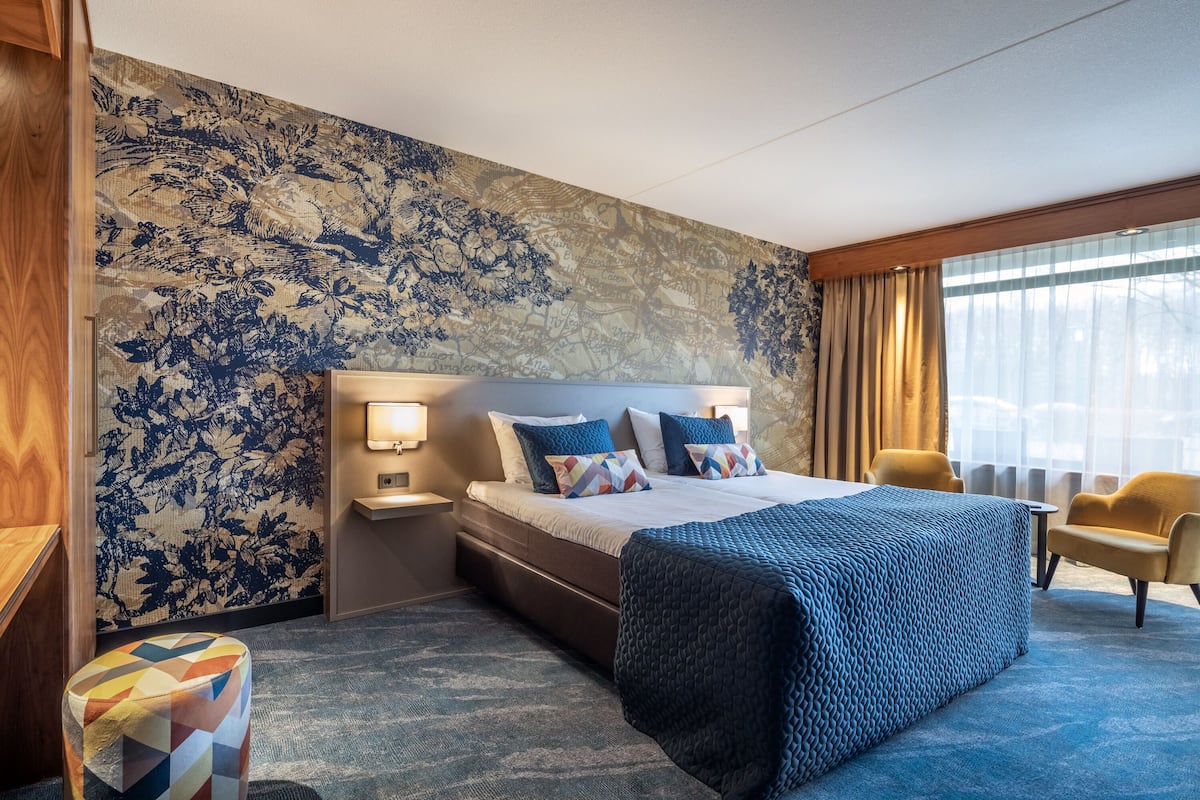 Habitación de hotel con una cama grande, una mesita de noche, una silla y un papel tapiz con motivos florales.