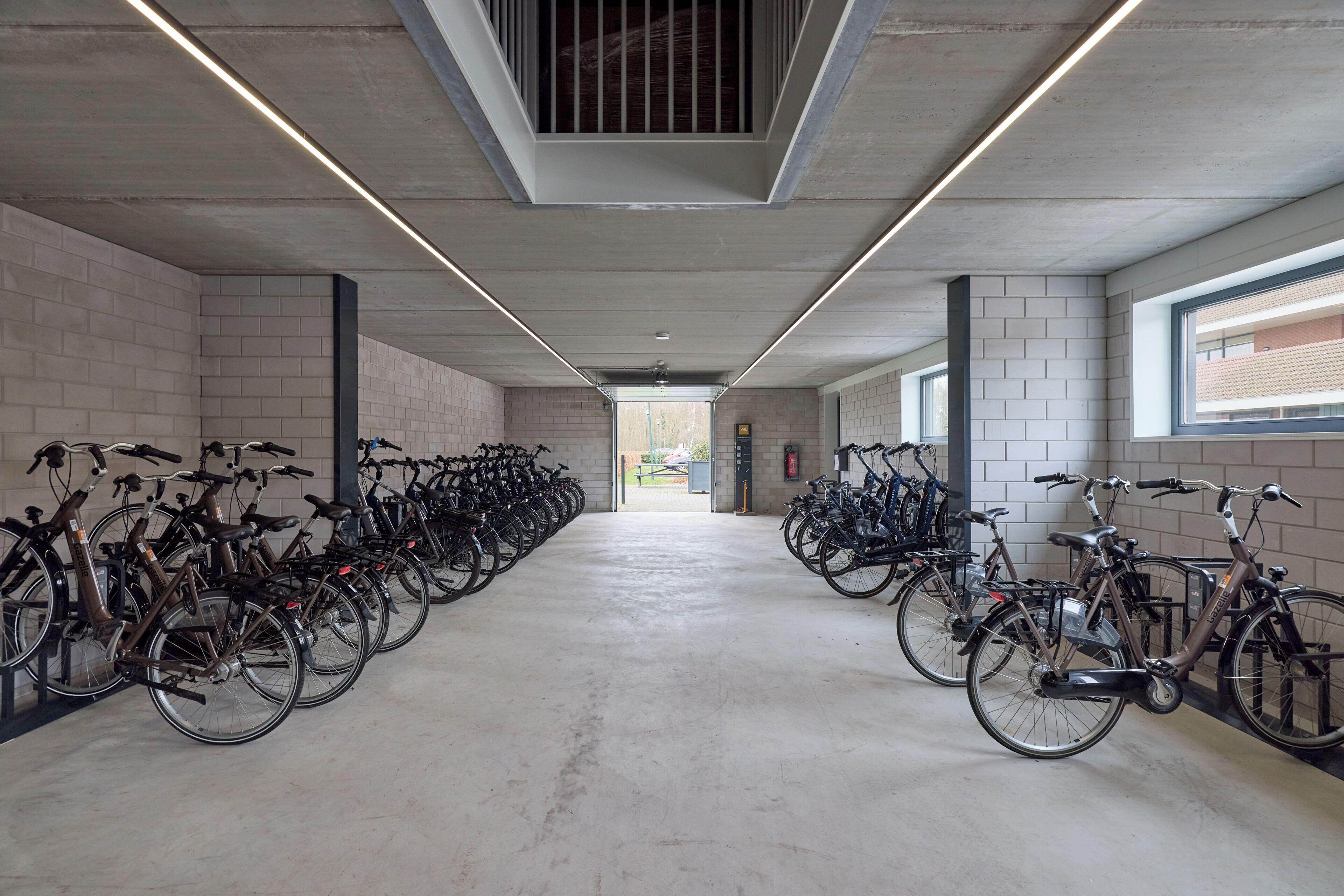 A bike rental station with rows of bicycles, concrete walls, and a long corridor.