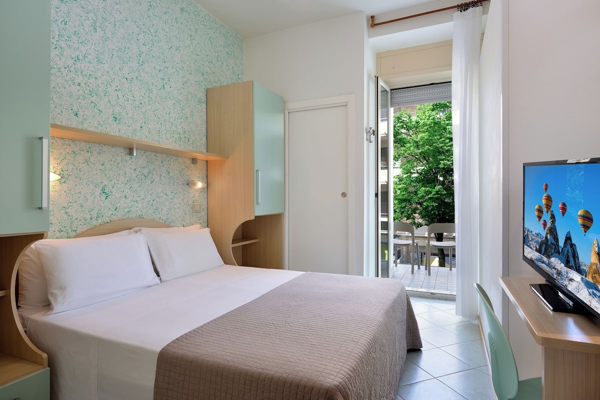 Habitación de hotel con cama, televisión, escritorio y vistas al exterior.
