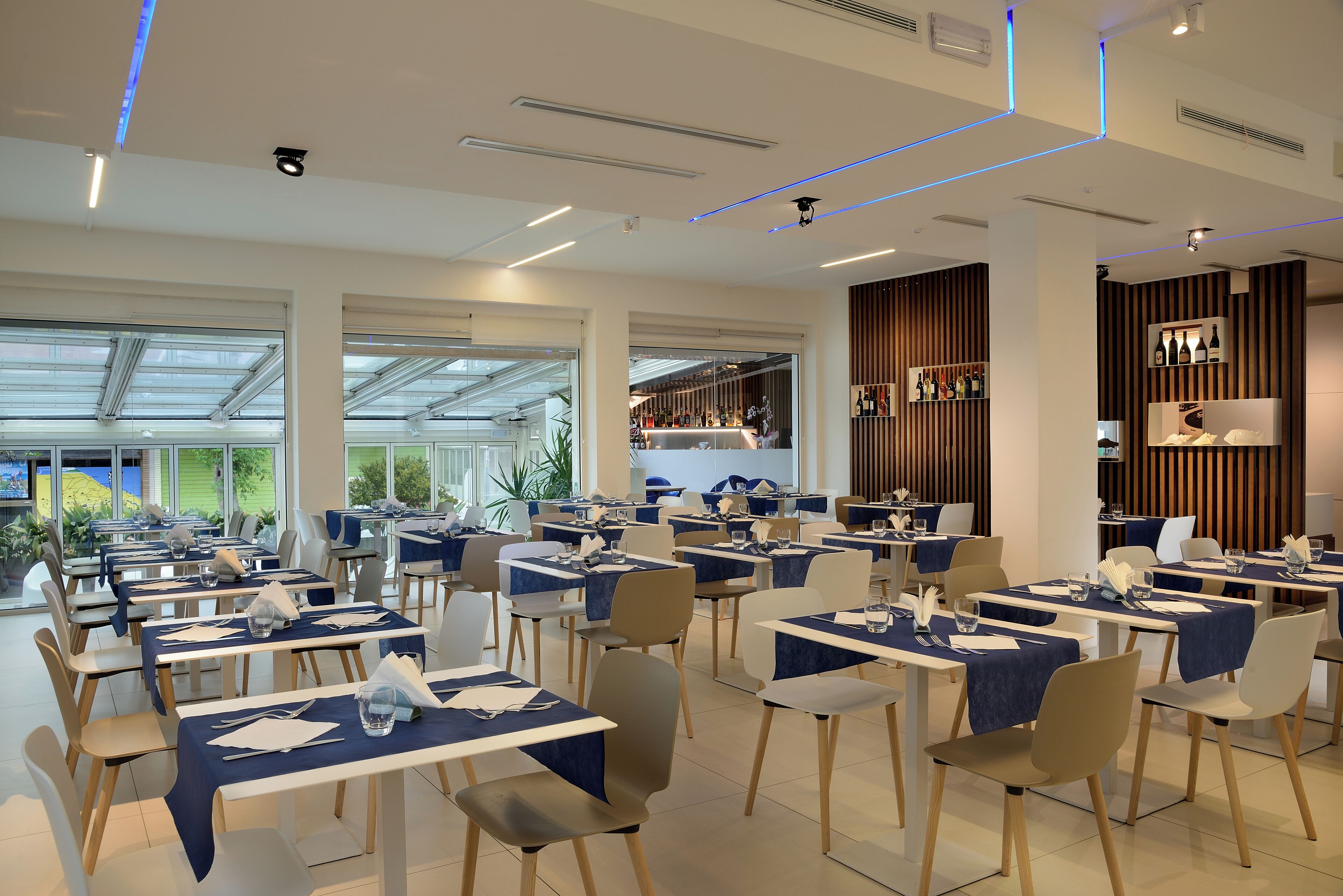 A modern restaurant with tables set for dining, a bar area, and large windows offering a view of the outdoors.