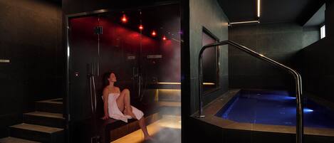 Uma área de spa com hidromassagem, uma mulher sentada num banco e uma escadaria que dá para um sauna.
