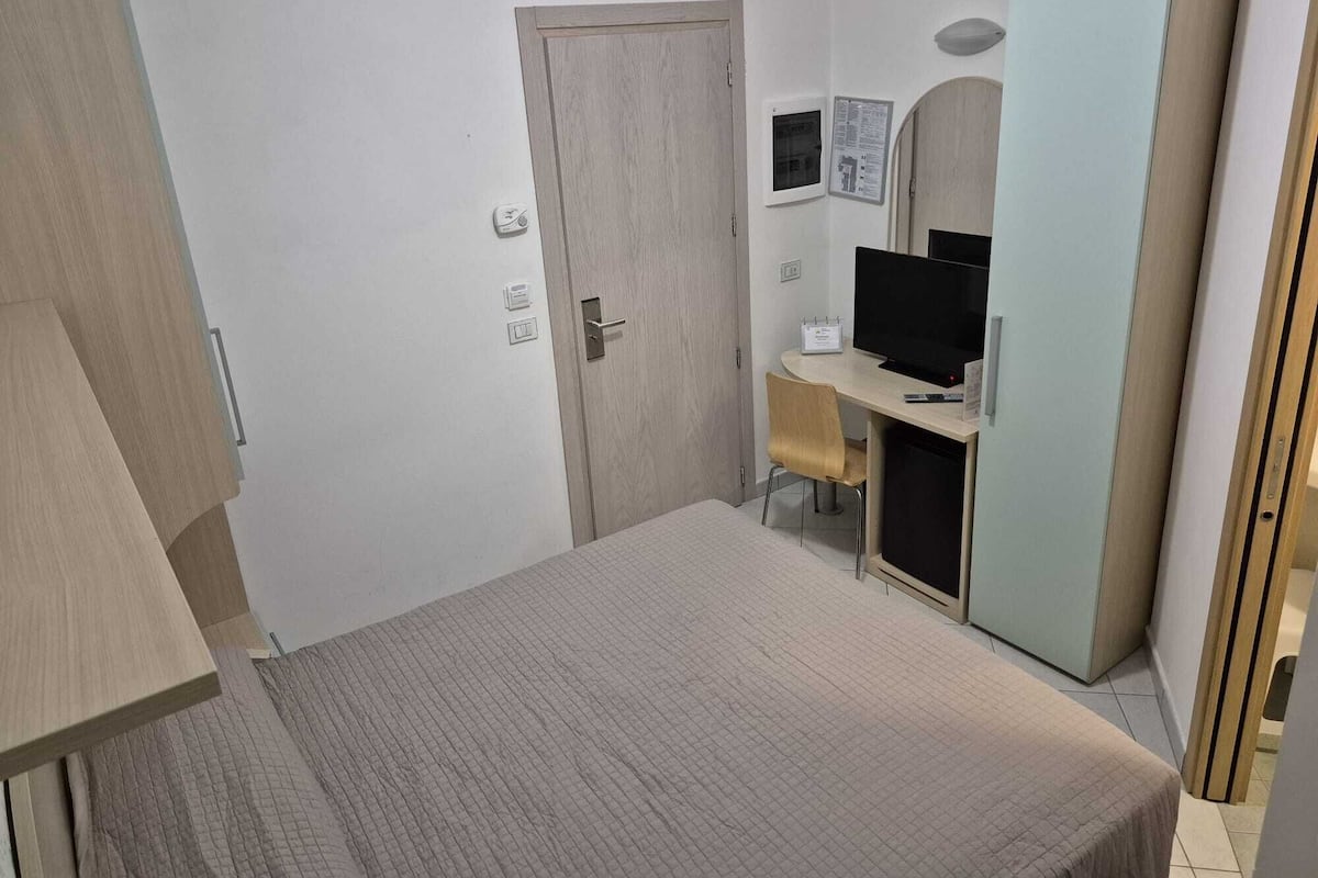 Un dormitorio con cama, escritorio con computadora, silla y armario.