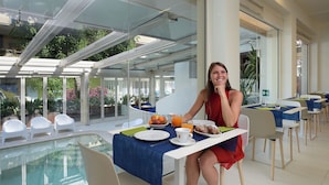 A dining area with a pool view, tables with blue tablecloths, and a glass-enclosed space. - Hotel Romagna (Cattolica)