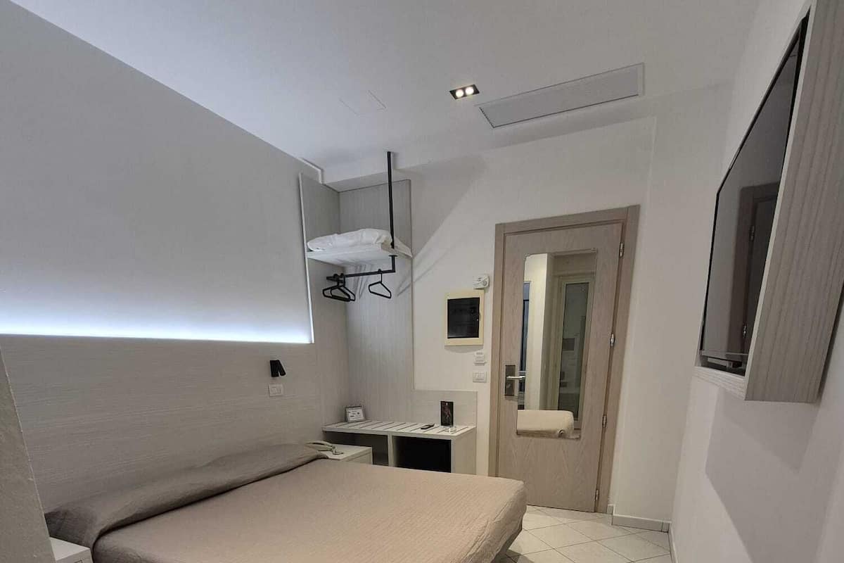 Un dormitorio moderno con cama, mesita de noche, escritorio pequeño, espejo y armario.