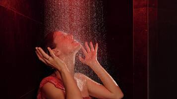 Una persona con un vestito rosso, con le mani alzate, circondata da una nuvola d'acqua.
