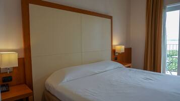 Quarto de hotel com uma cama grande, duas mesas de cabeceira com abajures e vista para o verde pela janela.