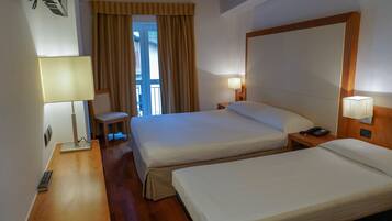 A hotel room with two beds, a chair, a desk, a lamp, and a phone.