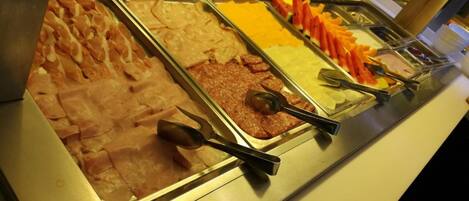 A buffet with various food options including meats, cheeses, and fruits.