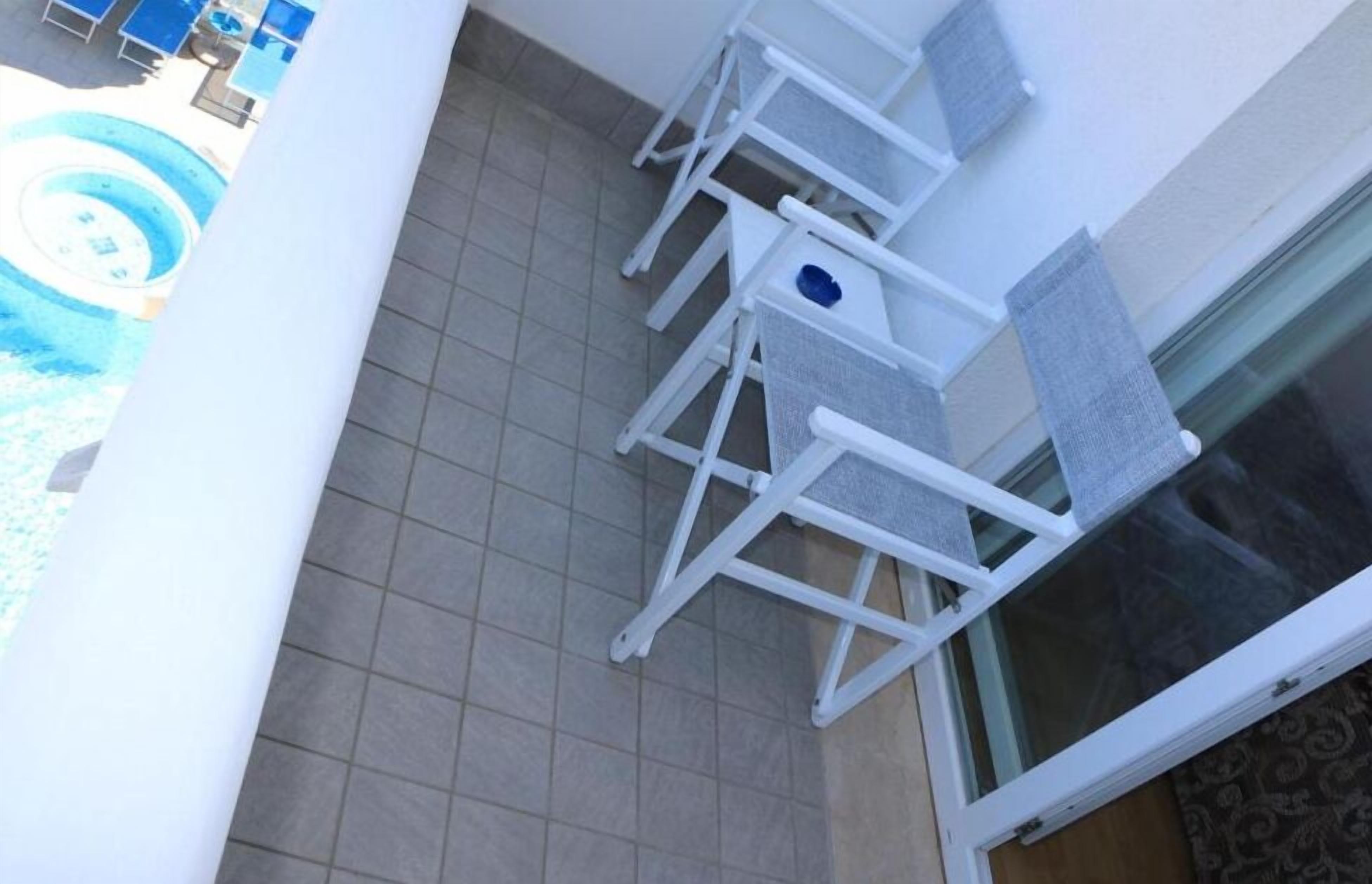 Un patio empedrado con sillas blancas y una mesita, con vistas a una piscina.