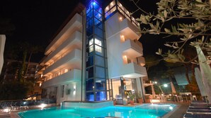 Un hotel moderno con zona de piscina, varios balcones y fachada bien iluminada.
