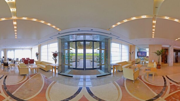 A spacious lobby with a curved floor design, a glass entrance, and a seating area with sofas and tables. - Hotel Tiffany (Trezzano sul Naviglio)