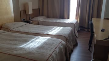 A hotel room with two beds, a desk, a lamp, and a TV.