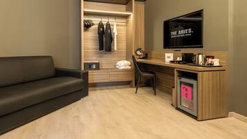 Una habitación de hotel moderna con sofá, escritorio con cafetera, televisión y refrigerador pequeño.