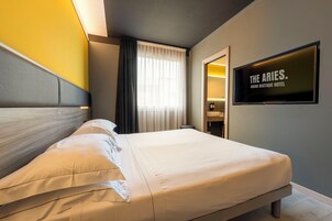 Una habitación de hotel con cama, televisor montado en la pared y ventana con cortinas.