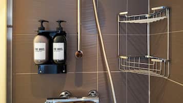 A bathroom with two bottles of The Aries hair conditioner and body wash, a chrome shower control, and a metal shower tray.