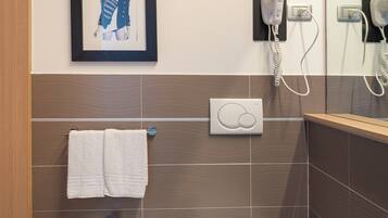 Un baño moderno con un bidé, un inodoro, un perchero para toallas y una obra de arte enmarcada en la pared.