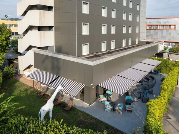 A modern building with a flat roof, multiple windows, and a covered outdoor seating area with chairs and tables. - The Aries Hotel (Vicenza)