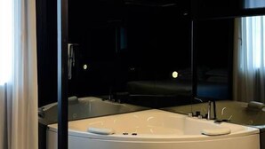 A modern bathroom with a large bathtub, a mirror, and a window with curtains. - The Aries Hotel (Vicenza)