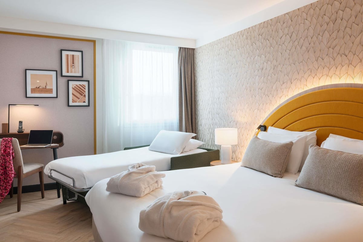 Ein Hotelzimmer mit zwei Betten, einem Schreibtisch mit einem Laptop, einer Lampe und gerahmten Bildern an der Wand.