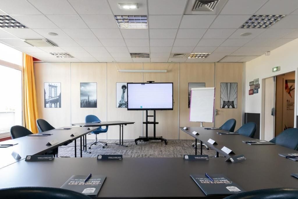 Un salón de conferencias con una gran mesa, sillas, una pantalla de proyector y una pizarra.