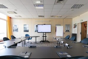 Une salle de conférence équipée d’une grande table, de chaises, d’un écran de projection et d’un tableau blanc.